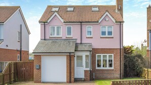 A two-story pink house with a garage, a brick facade, and a tiled roof. - Discover coastal bliss at The Dunes, your perfect family haven by Beadnell Bay. (Beadnell)