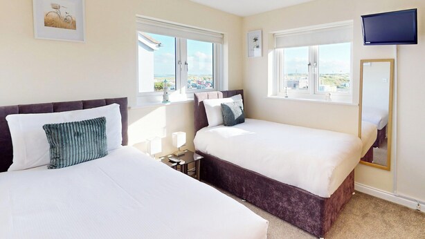 A hotel room with two beds, a TV, and large windows with a view. - Discover coastal bliss at The Dunes, your perfect family haven by Beadnell Bay. (Beadnell)