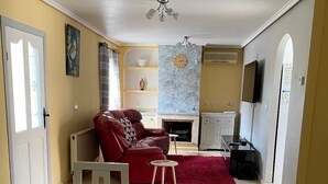 Una sala de estar con un sofá rojo, un sillón blanco, una mesita y una chimenea.