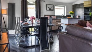 Une cuisine moderne dotée d’un îlot central, un coin repas avec une table dressée pour six personnes et un salon avec un canapé.