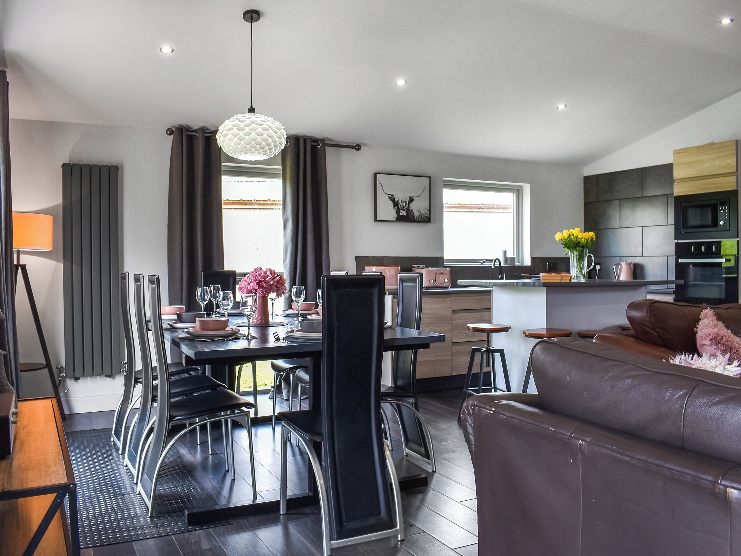 A modern kitchen with a central island, a dining area with a table set for six, and a living area with a sofa. - 4 bedroom accommodation in Kirkby Lonsdale (Kirkby Lonsdale)