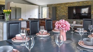 Uma sala de jantar moderna com uma mesa preta posta para seis pessoas, rodeada por cadeiras escuras. Um vaso rosa com flores está sobre a mesa.