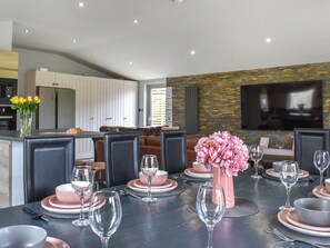 A modern dining area with a black table set for six, surrounded by dark chairs. A pink vase with flowers is on the table.