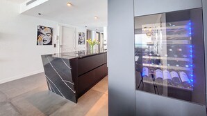 Une cuisine moderne dotée d’un îlot en marbre, d’un meuble à vin avec des bouteilles éclairées et d’œuvres d’art accrochées aux murs.