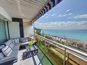 En balkon med sofa, sofabord og udsigt over stranden og havet.