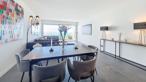 Un espace de restauration moderne, doté d’une grande table, de chaises et offrant une vue sur l’océan grâce à une vaste fenêtre.