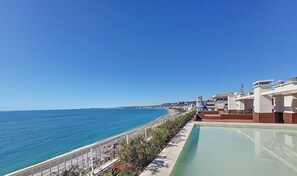 A swimming pool adjacent to a beach with a clear view of the ocean.