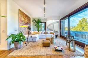 Uma sala de estar moderna com um sofá branco, uma grande planta em vaso, um tripé e uma escada em espiral.