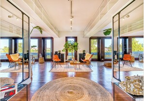 Uma sala de estar ampla com grandes janelas, uma planta central e móveis modernos.