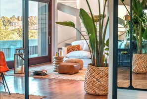 A modern living room with a large window, a sofa, a coffee table, and a potted plant.