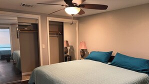 Un dormitorio con una cama, ventilador de techo, mesita de noche con lámpara y armario.