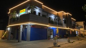 A two-story building with a sign for 'BIMAR' on the ground floor, a balcony on the upper floor, and a blue shuttered entrance.