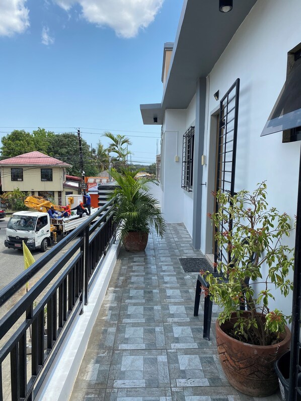 A balcony with potted plants, a tiled floor, and a view of the street.