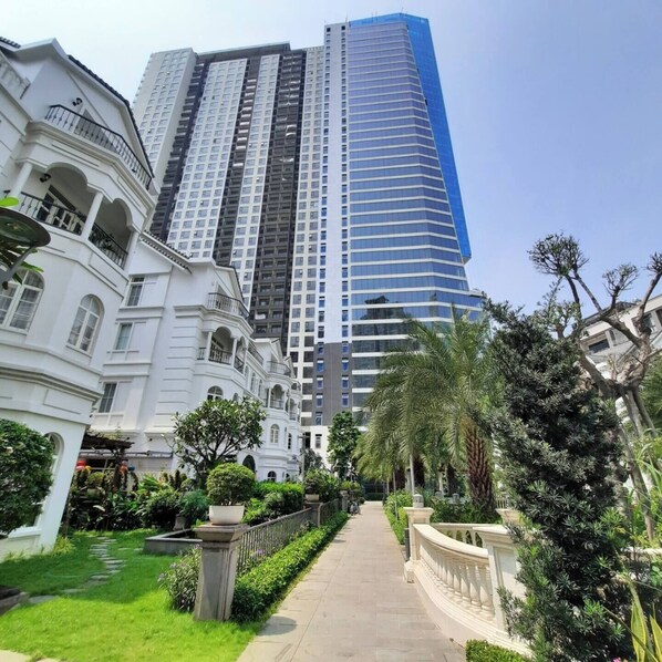 A pathway flanked by lush greenery and a tall modern building with a blue facade.