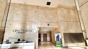 Un vestíbulo moderno de hotel con una recepción, un cartel con la letra 'B' grande y un cartel publicitario del hotel.