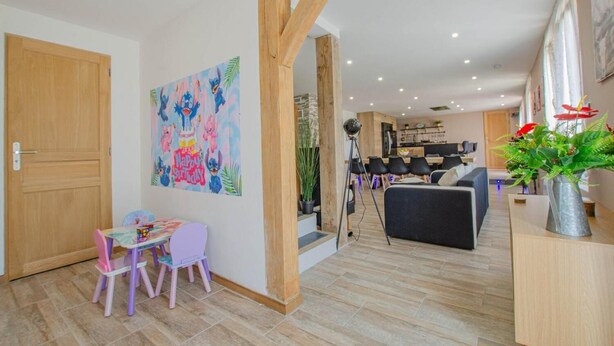 Un espacio habitable moderno con una puerta de madera, un adorno de pared colorido, una zona de comedor con mesa y sillas, y una cocina al fondo.