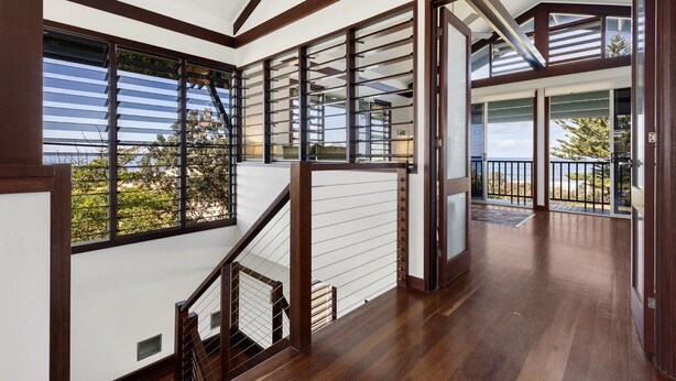 A spacious interior with a wooden staircase, large windows, and a balcony with a view of the sea. - Allawah Cottage - Historic Beachside Retreat With Pippi Beach Views - Holiday Yamba (Yamba)