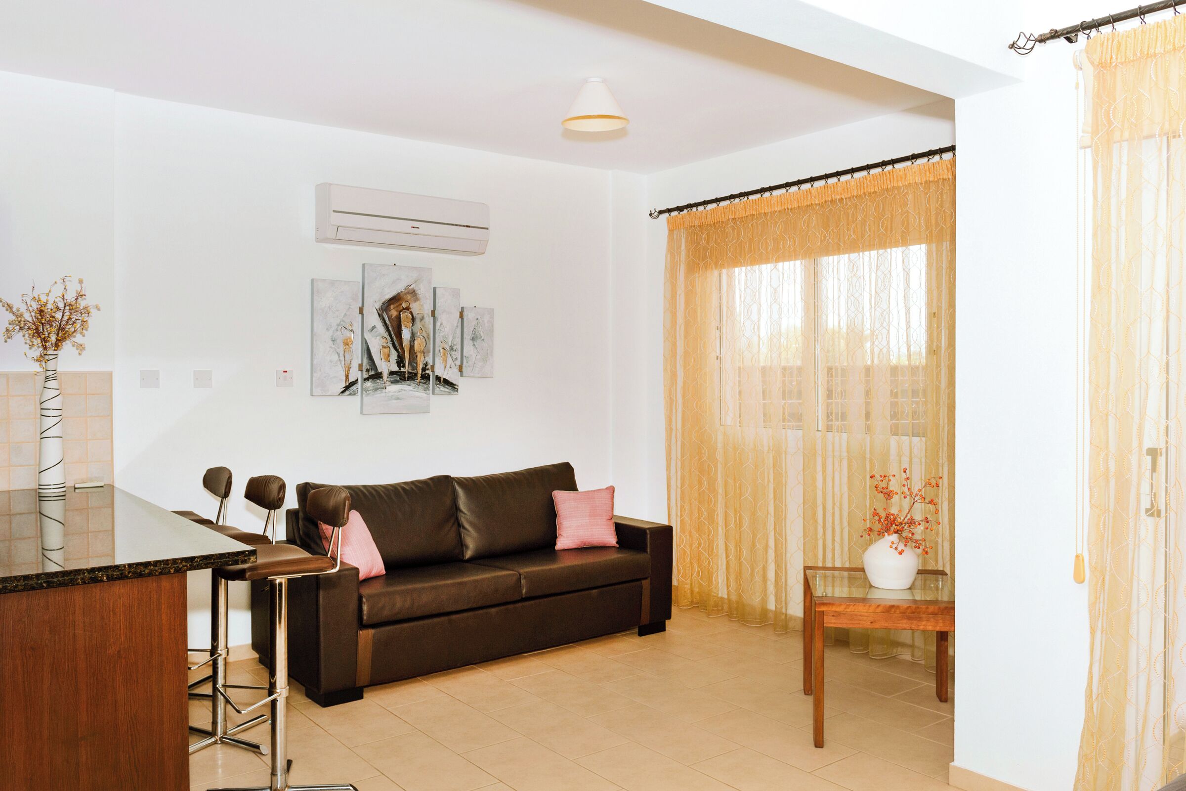 A modern living room with a brown leather sofa, a glass-top coffee table, and a small wooden side table with a vase.