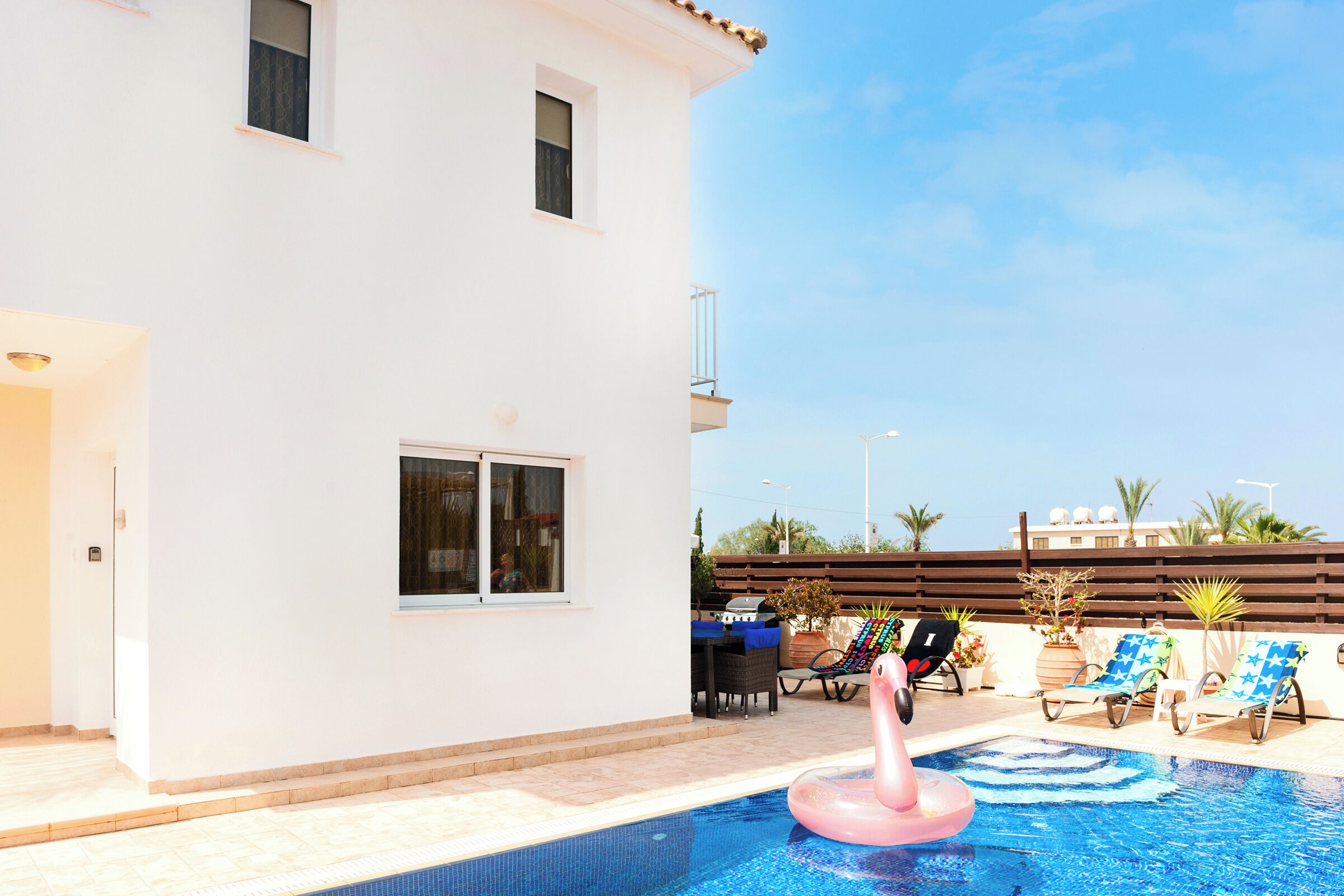 A swimming pool with a pink flamingo float, lounge chairs, and a barbecue area.
