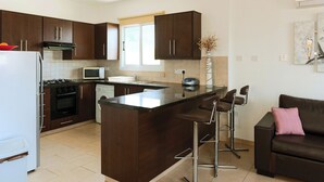 A modern kitchen with dark wooden cabinets, a central island with bar stools, a white refrigerator, a stove, and a microwave. - Great 3 bedroom villa, with private pool, in the best location in Protaras (Protaras)