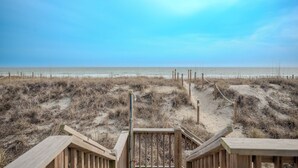 A wooden staircase leading to a beach with a clear sky. - Dreamy Days: Coastal Cottage with Awe-inspiring Oceanfront Setting (Oak Island)