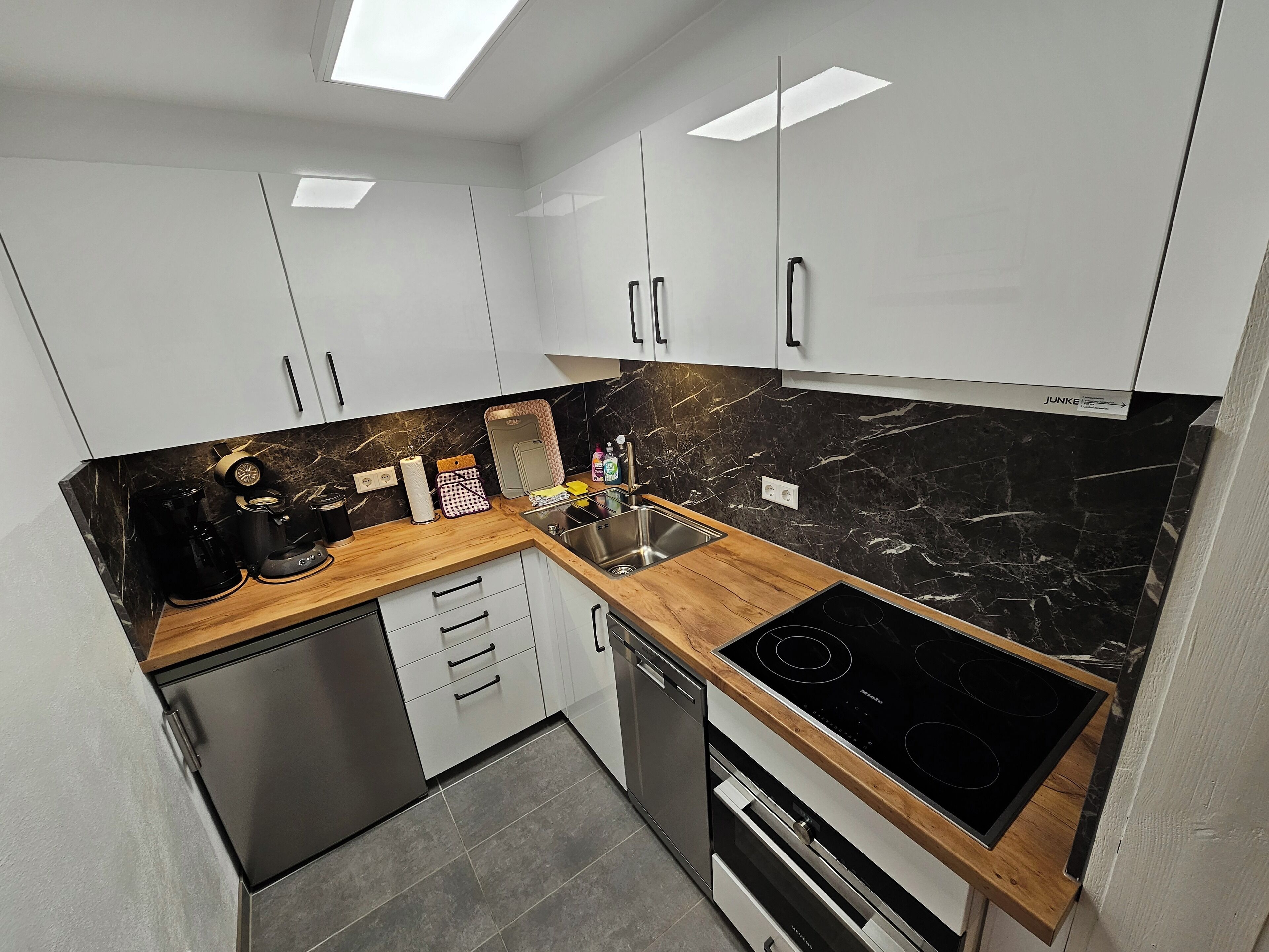 A modern kitchen with white cabinets, a black marble backsplash, a wooden countertop, and stainless steel appliances including a dishwasher, oven, and stove.