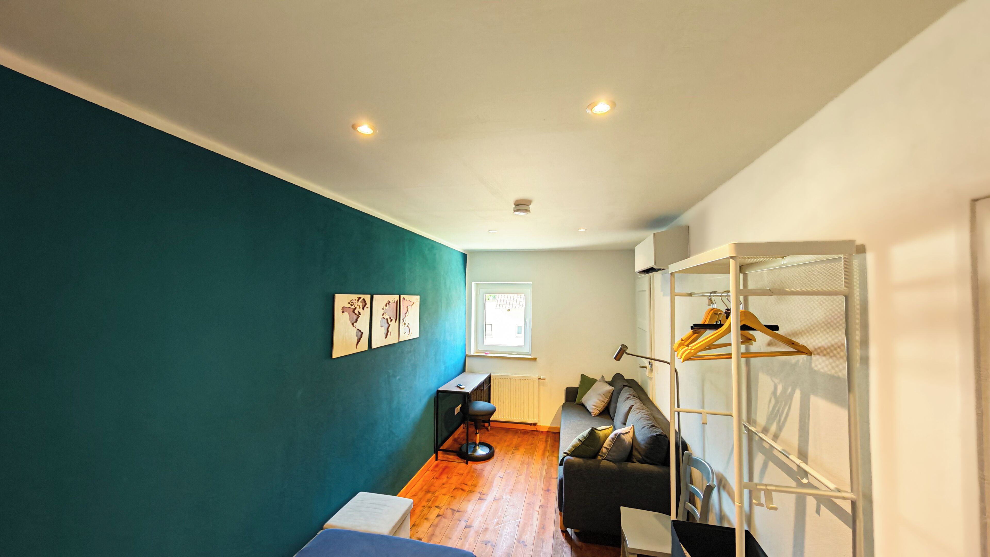 Un espace de vie moderne avec un mur de couleur turquoise, un canapé, une petite table, un radiateur et un porte-vêtements.