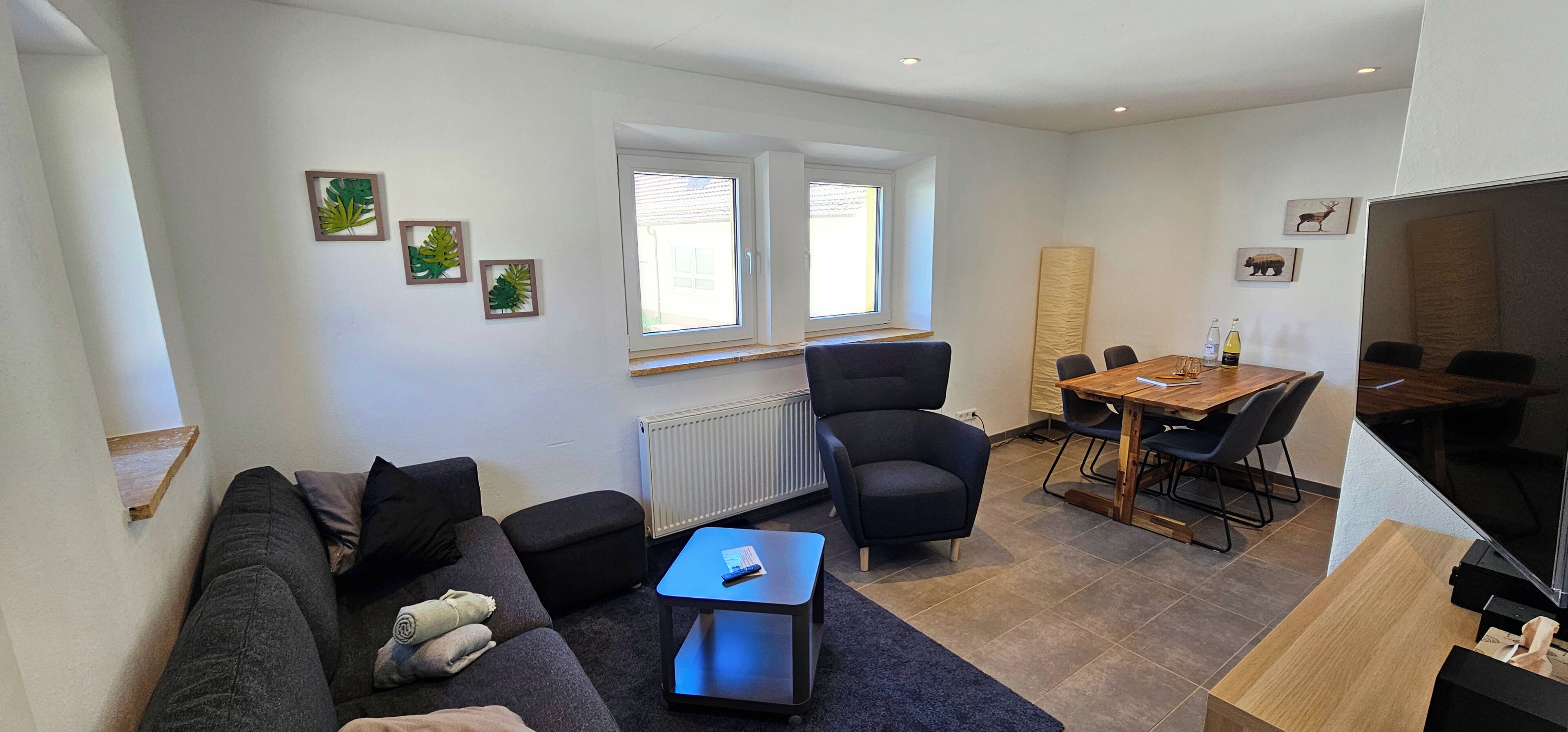 En moderne stue med sofa, sofabord, fjernsyn og spiseområde med bord og stole.
