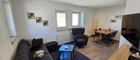 En moderne stue med sofa, sofabord, fjernsyn og spiseområde med bord og stole.