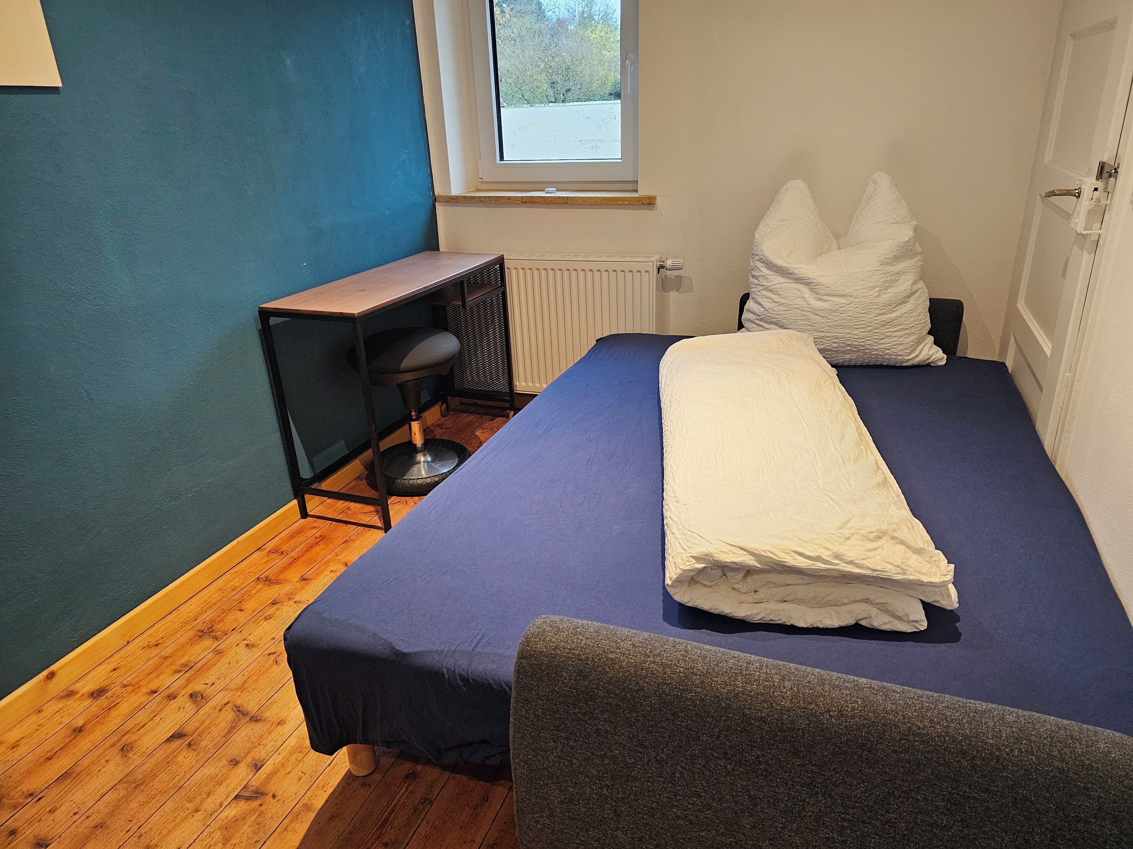 A bedroom with a bed, a desk, and a chair.
