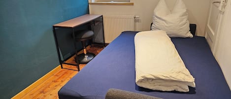 A bedroom with a bed, a desk, and a chair.