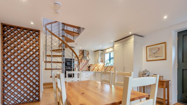 A modern kitchen with a wooden dining table, white chairs, and a spiral staircase. - 1 bedroom accommodation in Broad Chalke (Broad Chalke)