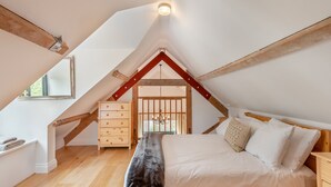 A bedroom with a sloped ceiling, wooden beams, a bed with white bedding, a dresser, and a window. - 1 bedroom accommodation in Broad Chalke (Broad Chalke)