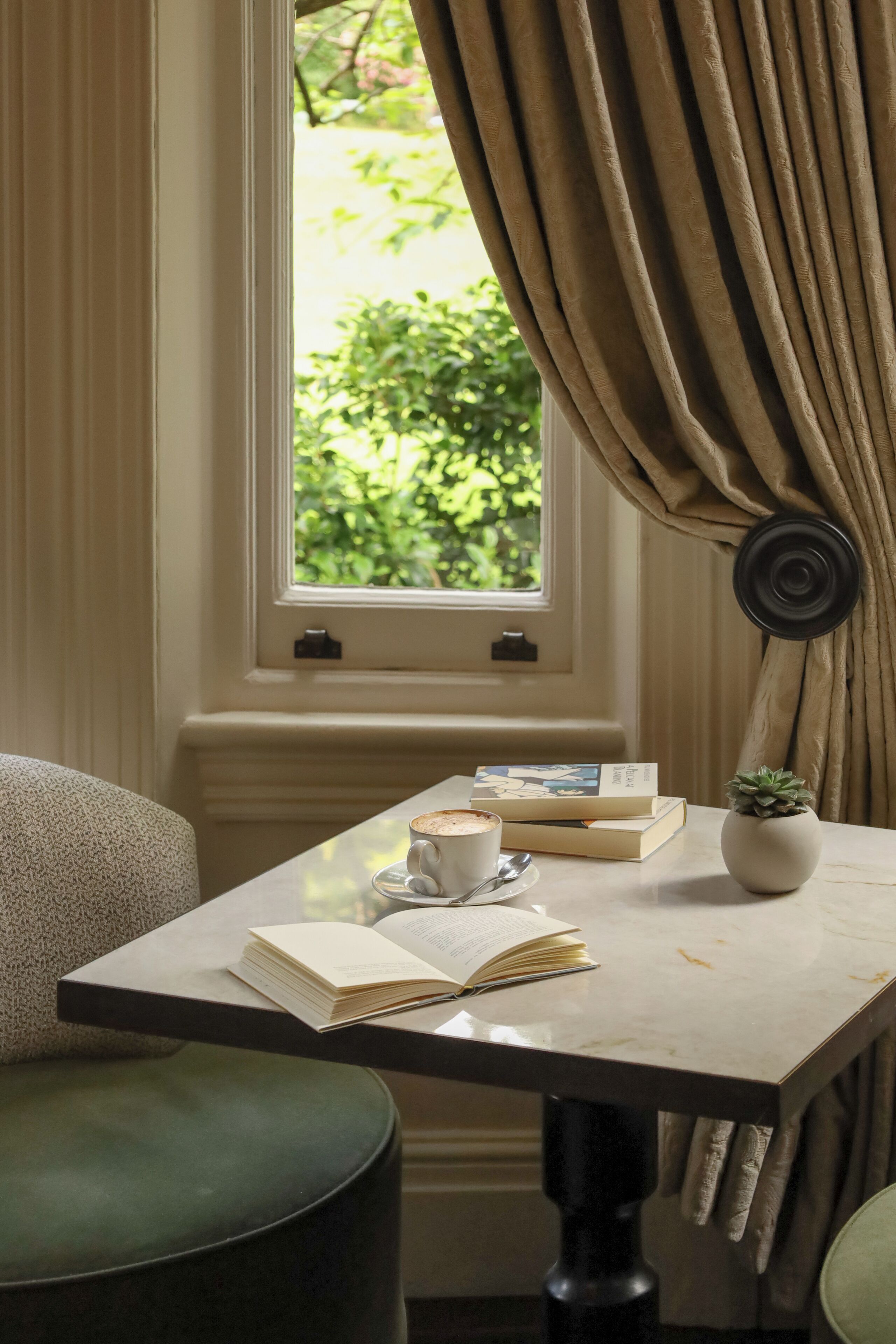 A cozy reading nook with a table, books, a cup of coffee, and a potted plant.
