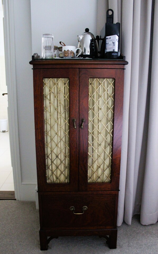A wooden cabinet with two glass doors, a kettle, a mug, and a coffee maker on top. - The Chelsea Townhouse (London)