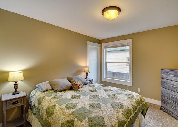 A bedroom with a bed, two bedside lamps, a dresser, and a window with blinds.