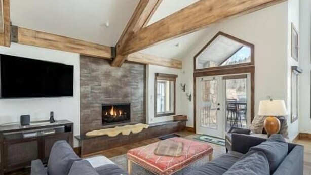 A cozy living room with a fireplace, a large flat-screen TV mounted on the wall, and a comfortable seating area with a sofa and ottoman. - Misty Maiden Vista (Telluride)