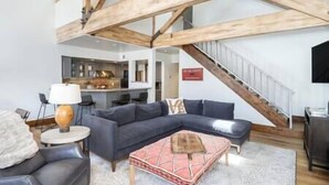 A modern living room with a dark grey sectional sofa, a round coffee table, and a staircase leading to an upper level. - Misty Maiden Vista (Telluride)