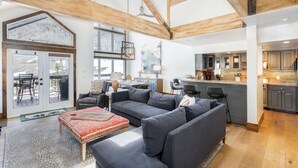 A spacious living area with a large gray sectional sofa, a red patterned coffee table, and a wooden ceiling with exposed beams. - Misty Maiden Vista (Telluride)
