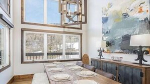 A dining area with a long wooden table set for six, large windows, and a modern abstract painting on the wall. - Misty Maiden Vista (Telluride)