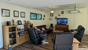 A living room with a sofa, two armchairs, a coffee table, a TV, and a wooden cabinet with shelves. - Oak Cottage - Daylesford - 200m from everything (Daylesford)