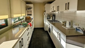 A modern kitchen with white cabinets, stainless steel appliances, and a variety of utensils hanging on the wall. - Oak Cottage - Daylesford - 200m from everything (Daylesford)