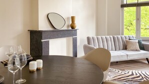 A modern living room with a round dining table, a sofa, a fireplace, and a large window with a view of greenery. - Stylish Apartment in Centre of Maastricht (Maastricht)