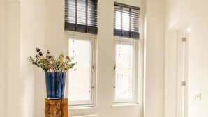 A room with two windows, a wooden stool with a vase of flowers, and a white door. - Stylish Apartment in Centre of Maastricht (Maastricht)