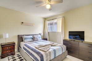 Ein Schlafzimmer mit Bett, Kommode, Fernseher, Deckenventilator und einem Fenster mit Vorhängen.