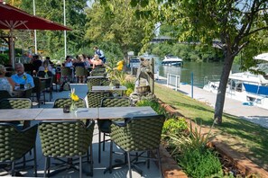 An outdoor dining area with tables and chairs, a river view, and boats in the background. - Charming Rustic houseboat at Bray Marina (Windsor)