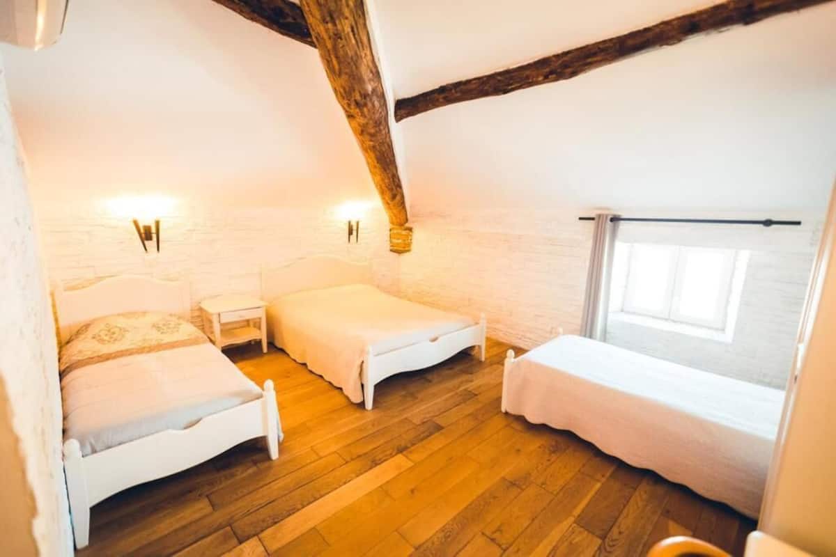 A room with two beds, a window, and a wooden ceiling beam.