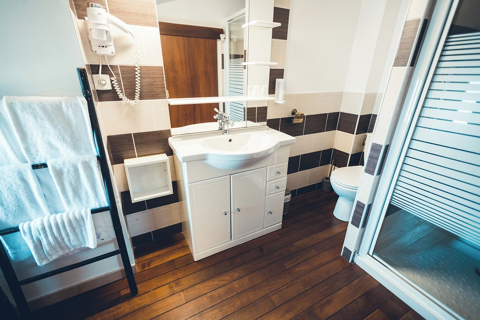 Un baño moderno con suelo de madera, lavabo blanco y un inodoro.