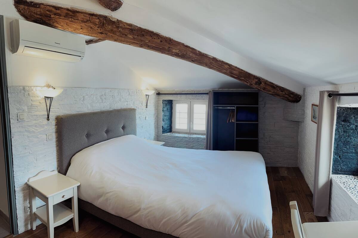 A bedroom with a large bed, a nightstand, a wardrobe, and a stone wall.