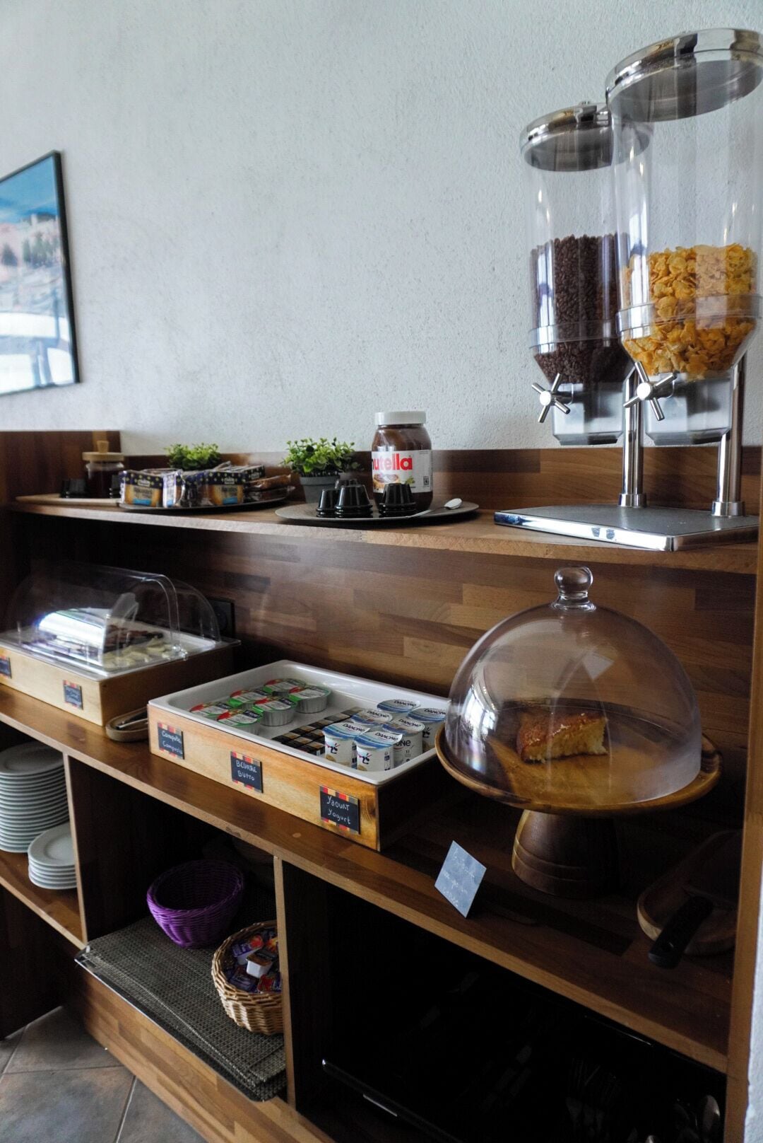 A breakfast buffet with various food items, including cereal, yogurt, and a covered pastry.